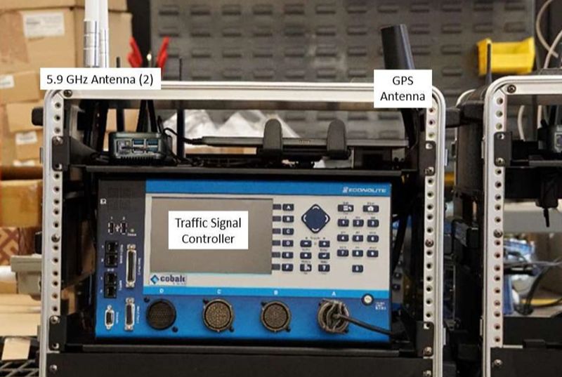 This photo is a front view of the Connected and Automated Vehicle education (CAVe)-in-a-box infrastructure kit. Two 5.9 gigahertz (GHz) antennas, the GPS antenna, and the traffic signal controller are labeled at their respective locations.