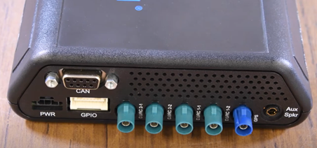 A photo of the connection ports on an onboard unit (OBU). The OBU pictured has nine ports and are labeled as such (from left to right): PWR, CAN, GPIO, DSRC2-1, DSRC2-2, DSRC1-1, DSRC 1-2, GPS, and Aux Spkr.