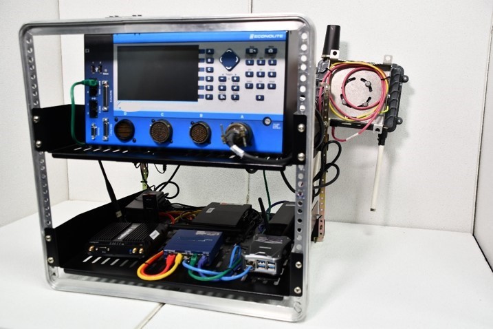 Photo depicts a two-tiered rack of equipment containing boxes and wires, including a large box on the top with several buttons and dials on it as well as a small monitor screen and ports where cables can be plugged in.