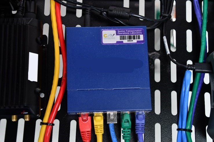 This photo shows a small, square metal box with four differently colored network cables entering ports at the bottom. The box is sitting on a computer rack.