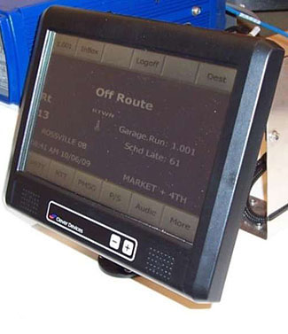 This is a photo of a small black touch screen device. Menu buttons appear on the top and bottom of the screen for a variety of functions such as Inbox, Logoff, Dest, Audio, and More. In the center of the screen it reads: Off Route, Rt 13, Garage Run: 1.001, Sched Late: 61.