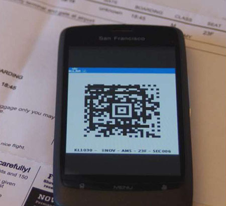 This is a photograph of a smart phone with a QR code displayed on the screen. There are papers like boarding passes behind the smart phone.