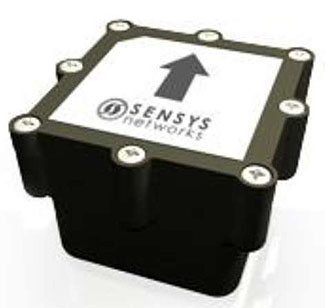 This is a photograph of a magnetometer from Sensys Networks. This device is a cube-like device. At the top of the device is the company logo and an arrow pointing up.