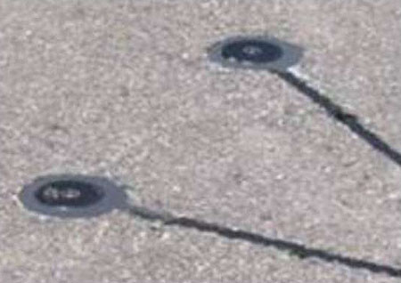 This is a photograph of Road Surface Sensors. The round disks and their connecting cables are embedded into the surface of the road in a V orientation.