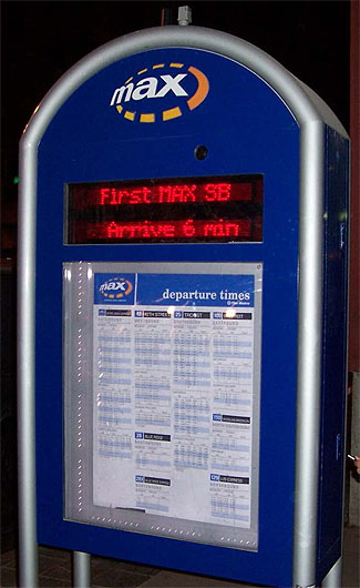 Example of En-route and Wayside Traveler Information displays. The image shows a blue kiosk with a built in message display. On the kiosk is a list of departure times. The message board reads "First MAX SB Arrive 6 min."