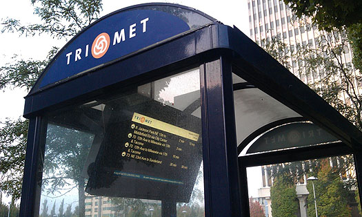 The photographs shows a large electronic display with destination and schedule information, mounted inside an outdoor transit kiosk.