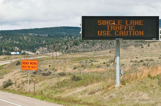 This is a photo to illustrate how ITS technology enhances Traveler Safety and Security. The photo shows an electronic road side along the right side of the road that reads: Single Lane Traffic. Use Caution.
