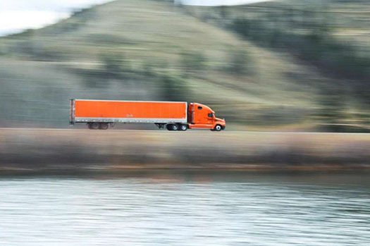 This slide represents how ITS technologies assist with Commercial Vehicle Operations. In the photo an 18-wheeler is driving along a lakeside road.