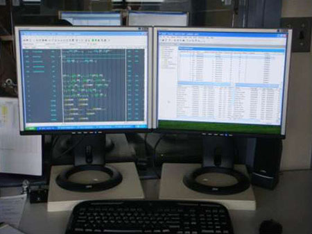 This photograph shows two computer monitors sitting on a desk side by side. The left monitor displays graphical data. The right monitor shows data and file displays.