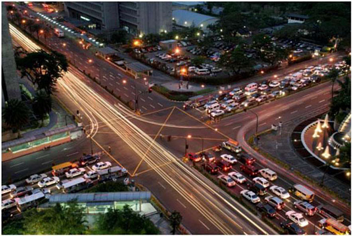 Time-lapse photo of a busy four-way intersection at dusk: Four lanes of traffic are stacked up in three directions at red lights; streaks of light along the fourth direction indicate traffic motion.