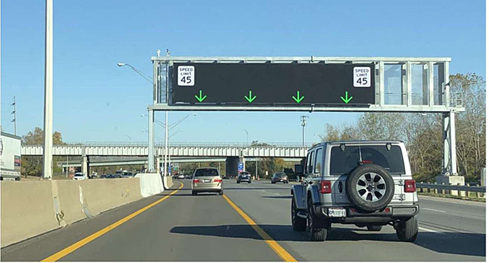 Photo of example SmartLane active traffic management with green arrows showing what lanes are open above a freeway with several vehicles on the roadway.