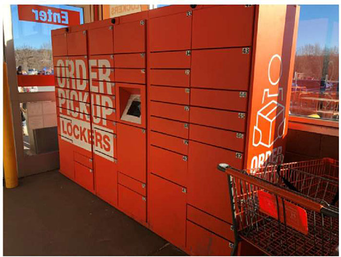 Photo of example order pickup boxes/lockers and related kiosk. Rows of lockers are stacked on top of each other in different columns with a computer terminal to provide access to unlock them.