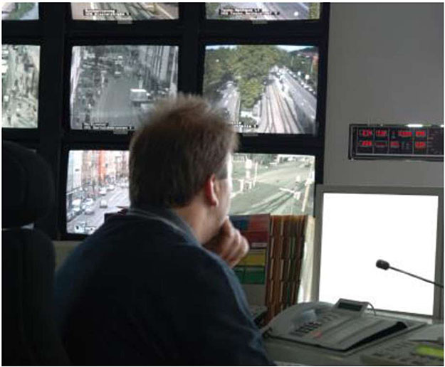 Photo of Traffic Management center with an operator viewing numerous screens of traffic cameras and a computer and phone system with microphone