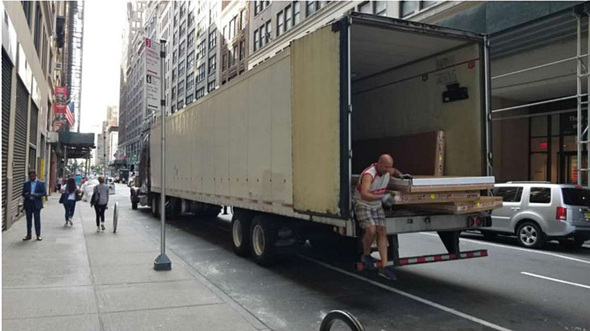 Photo of freight truck being loaded or unloaded on a busy city street with pedestrians nearby