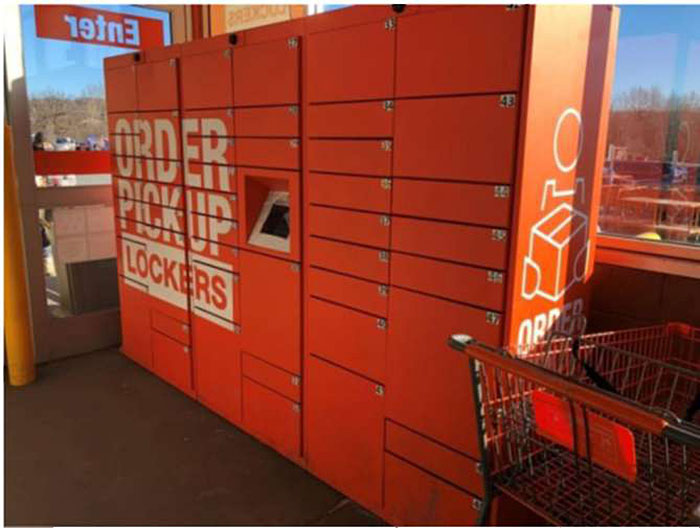 Photo of example order pickup boxes/lockers and related kiosk. Rows of lockers are stacked on top of each other in different columns with a computer terminal to provide access to unlock them.