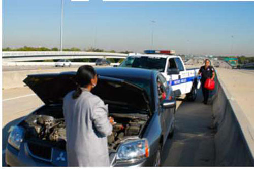 Photo showing a stranded motorist pulled over on the side of a roadway with engine problems, with someone coming to assist in a service truck.