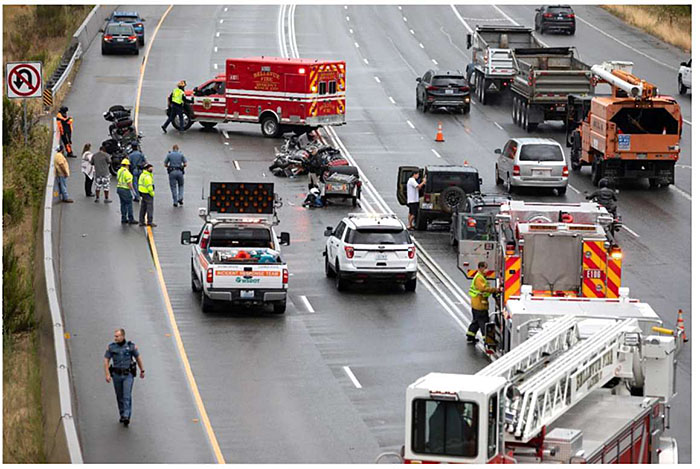 Photo of scene of a traffic incident on a major roadway involving multiple vehicles, an ambulance, firetruck, other emergency vehicles and various police and other emergency service personnel.