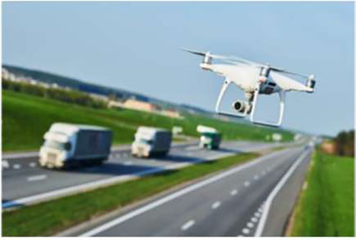 Stock photo of an unmanned aerial vehicle (UAV) or drone flying over a major roadway with trucks in the background.