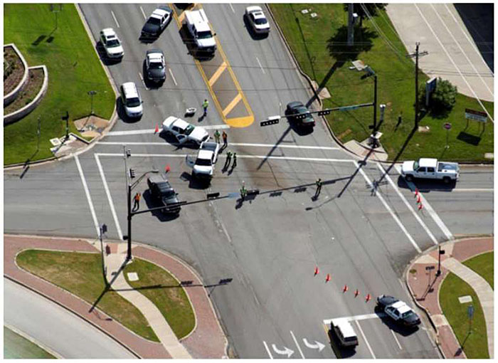 Aerial photo of an incident at an intersection of an arterial roadway with several vehicles, trucks, police vehicles, and police officers directing traffic, blocking lanes and using cones to direct traffic around the incident.