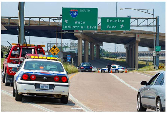 Photo example of exit ramp off freeway in Texas near 35E showing police and emergency vehicles managing traffic, with traffic cones used by a police officer in the distance.