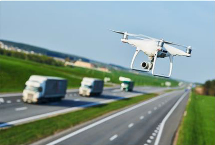 Stock photo of an unmanned aerial vehicle (UAV) or drone flying over a major roadway with trucks in the background.