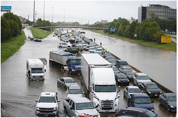 Photo from Texas A&M Transportation Institute showing major freeway system completely flooded with a truck mostly submerged and trapped in the water, with the city in the background.