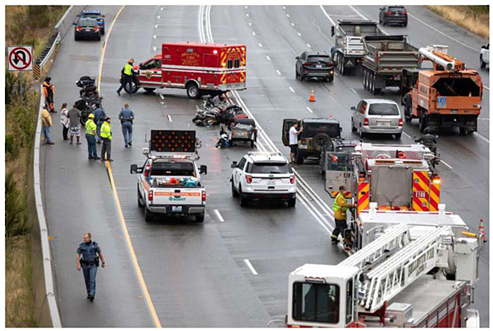 Photo of scene of a traffic incident on a major roadway involving multiple vehicles, an ambulance, firetruck, other emergency vehicles and various police and other emergency service personnel.