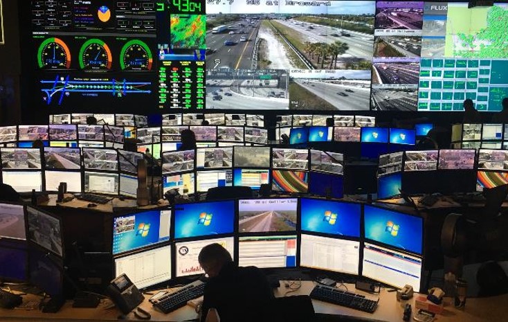 various ITS-related icons superimposed on an overhead photo of a highway interchange: a road, a satellite, a cloud, a traffic light, a bus, a pedestrian, a car, a road, etc.